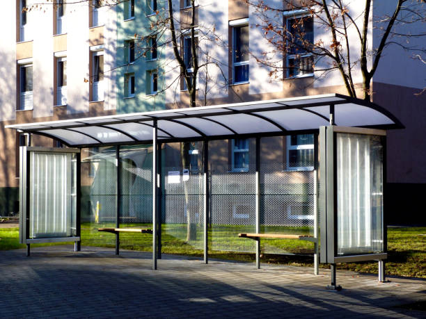 bus shelter at a bus stop of glass and aluminum structure in park like setting bus shelter at a bus stop of glass and aluminum structure in park like setting in day time with green background and appealing polka dot safety glass design and wooden benches & poster display glass bus shelter stock pictures, royalty-free photos & images