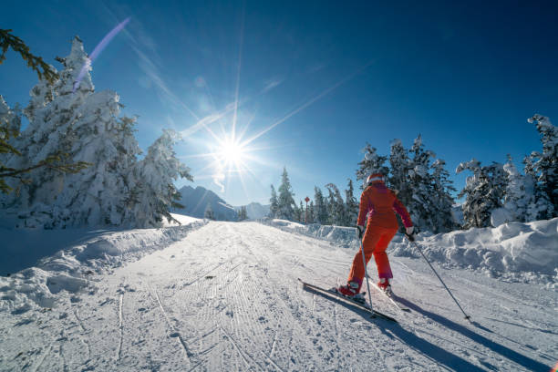 rear view skiing woman female skier pushing along flat connection ski piste slope path on sunny winter vacation day in mountains with starshapped sun and trees along covered with deep snow