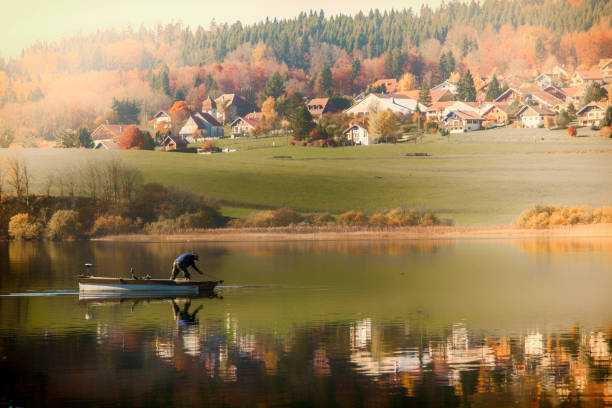 Lake of Saint-Point, Franche-Comté A fisherman in his boat in the wrinkle-free water of the mountain lake. Autumn mountain landscape. jura france stock pictures, royalty-free photos & images