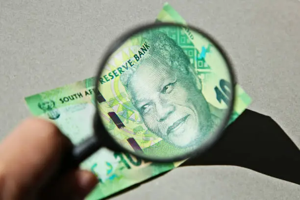 Photo of South African money concept image consisting of a magnifying glass and a 10 rand note.