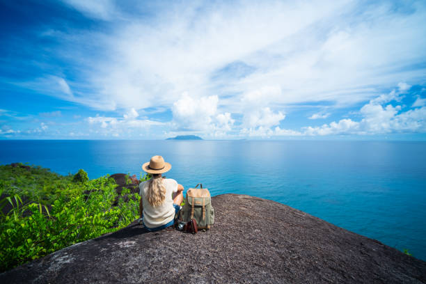 solo traveler back view one woman sitting on rock of tropical island enjoying seaview stock photo
