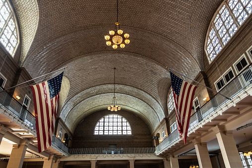 New York City, USA - August 1, 2018: The main building's registry room of the Ellis Island Immigration Station with two American flags in New York City, USA.