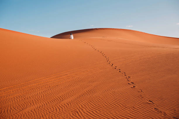 istock Man walks through the desert. Footprints on dunes. 1163181234