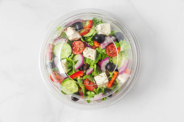 ensalada griega saludable en paquete de plástico para llevar o entrega de alimentos sobre un fondo de mármol blanco - packaging food plastic package fotografías e imágenes de stock