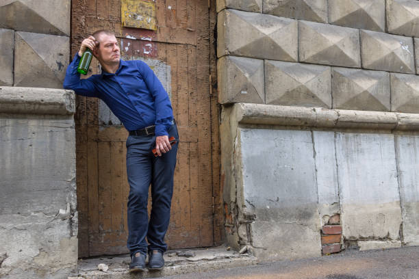 un homme ivre se tient dans l'allée avec une bouteille de boisson alcoolisée et regarde nerveusement les passants - eastern european caucasian one person alcoholism photos et images de collection