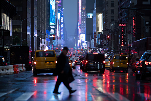 Person crossing the street in the rainy reflections of city lights from Times Square, New York City.