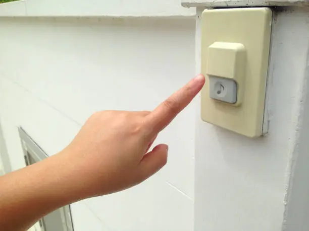 Woman's hand push the doorbell in front of house. Doorbell for guest in front of the house.
