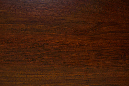 The wood is red and brown color with layers and lines like a rose petal. High angle view of a flat textured wooden board backgrounds. It has a beautiful nature and abstractive pattern. A close-up studio shooting shows details and lots of wood grain on the wood table. The piece of wood at the surface of the table also appears rich wooden material on it, shows elegant and soft textured. Flat lay style.