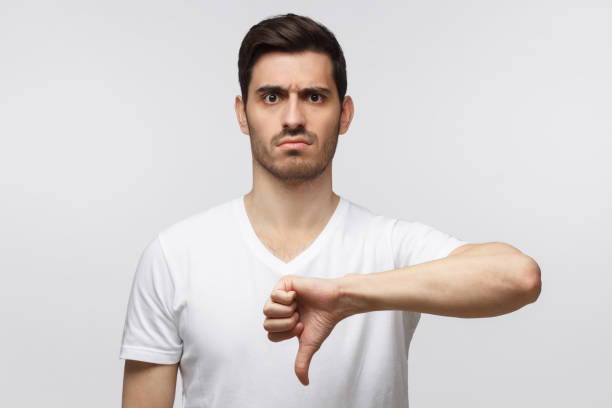 istock Disgruntled grumpy dissatisfied annoyed unhappy young man showing thumb down as dislike gesture isolated on gray background 1163192168
