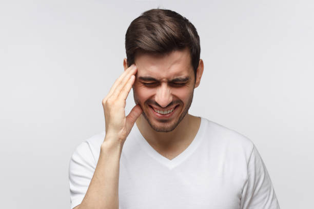istock Headache concept. Young man showing how much his head hurts, experiencing pain, looking miserable and exhausted, isolated on gray background 1163192213