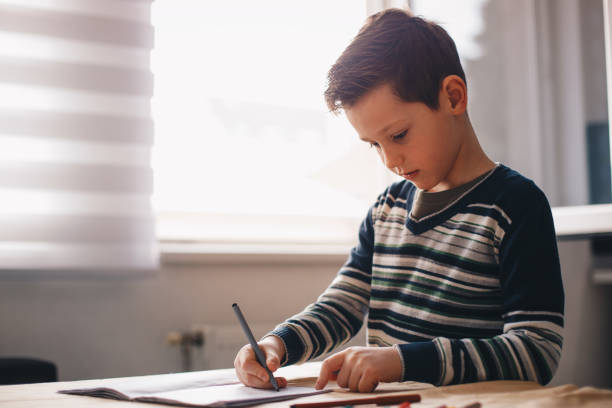 istock Young boy sitting at the table doing his school homework. 1163192784
