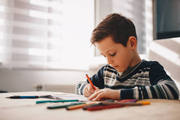 istock Young boy sitting at the table doing his school homework. 1163192817