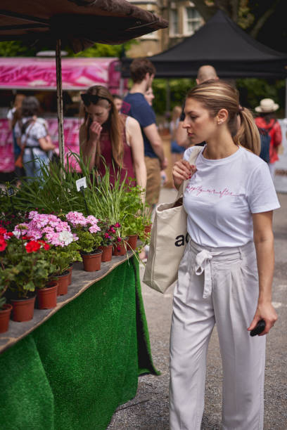 giovani che fanno shopping di fiori e piante in una bancarella di fiori nel mercato di brockley, un mercato contadino locale che si tiene ogni sabato nel sud-est di londra. - southeast england foto e immagini stock