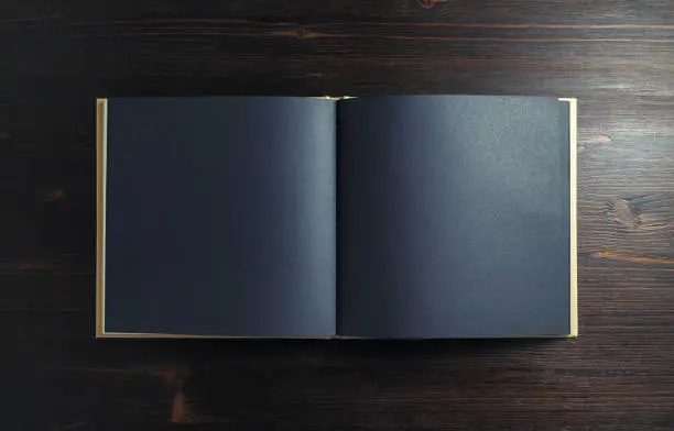 Photo of blank black booklet or brochure on dark wood table background. Copy space for text. Flat lay.