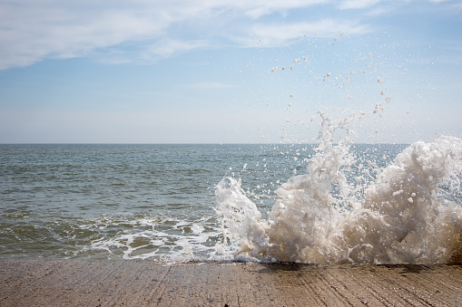 Splash. Sea water breaching coastal flood defence. Wave power background image. Fast shutter speed freezing droplets of water in mid air. Blue sky ocean horizon copy-space.