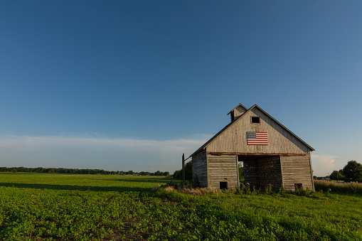 Old wooden barn in the Midwest with American Flag in the afternoon light.  LaSalle County, Illinois, USA