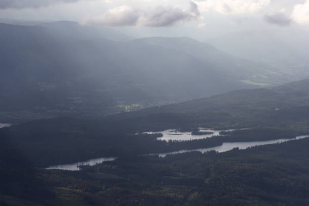 istock Dramatic view of bright sunlights going through clouds to land with forest 1163210855