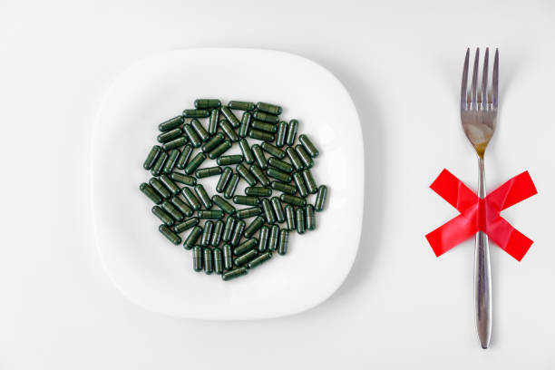 istock spirulina capsules on a white plate with fork and red cross on white background, dieting, detox, healthy lifestyle concept 1163211994