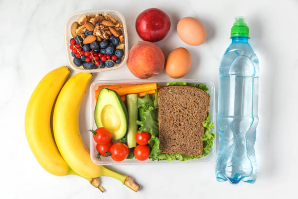 istock school lunch boxes with sandwich, vegetables, nuts, berries, banana, eggs, peaches and water on white marble background 1163217661