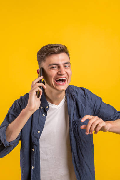 istock Handsome young man using his phone with smile while standing against yellow background.Young adult man talking on the phone scared in shock with a surprise face, afraid and excited with fear expressio 1163220162