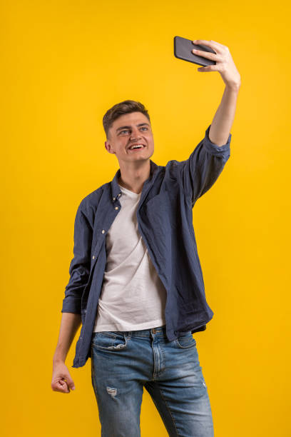 istock Cheerful young man wearing plaid shirt standing isolated over orange background, taking a selfie 1163220167