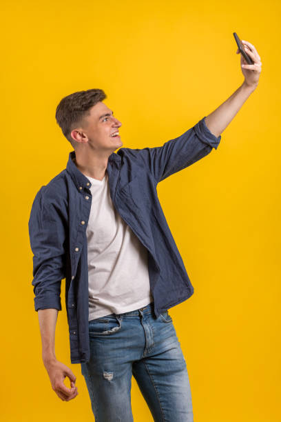 istock Cheerful young man wearing plaid shirt standing isolated over orange background, taking a selfie 1163220391