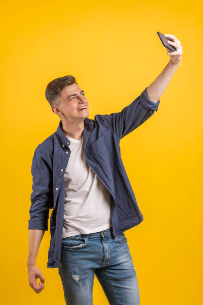 istock Cheerful young man wearing plaid shirt standing isolated over orange background, taking a selfie 1163220942
