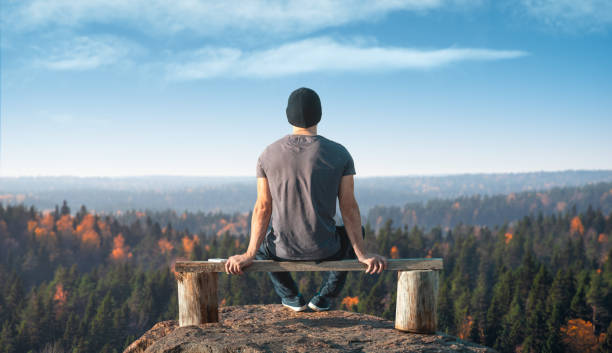 A man sits on a lookout point above the forest. Back view.