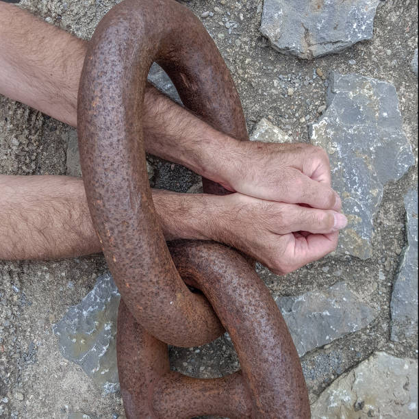 istock Hands in chains on the background of a stone wall. 1163226288