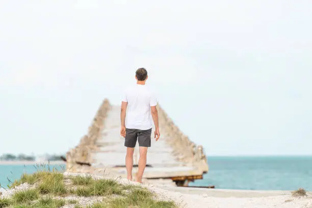 Young man standing in front of Old Seven Mile Bridge, Knights Key-Pigeon Key-Moser Channel-Pacet Channel, tourist on vacation, horizon seascape in Bahia Honda key in Florida, looking at sea, ocean