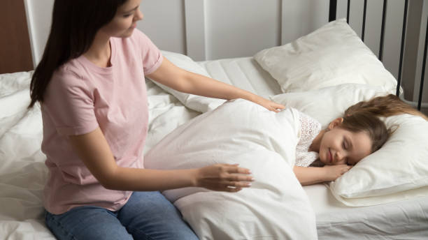 young mom caress little daughter put her to sleep - sleeping child bedtime little girls imagens e fotografias de stock