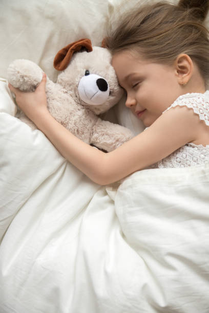 little girl sleep hugging teddy bear in white bedroom - sleeping child bedtime little girls imagens e fotografias de stock