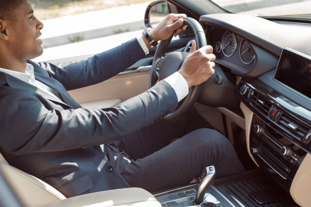 istock Young businessman driver sitting inside car holding steering wheel driving joyful side view 1163243445