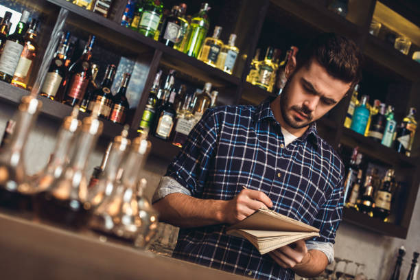 istock Young bartender standing at bar counter writing recipe in notebook thoughtful 1163243497