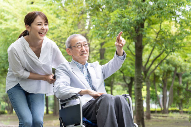 公園で車椅子を持つ若いアジアの女性と老人の男性 - 介護 ストックフォトと画像