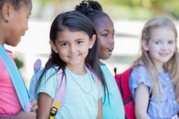 istock Beautiful Hispanic elementary age little girl smiles while standing outside with classmates 1163247755