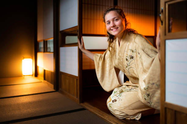 Traditional japanese house or ryokan with gaijin caucasian woman in kimono and tabi socks opening shoji sliding paper doors sitting on tatami mat floor stock photo