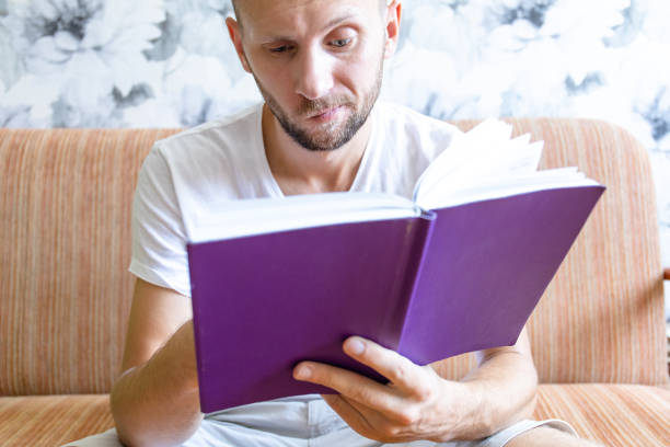 istock young guy reading a book at home sitting on the couch 1163249530