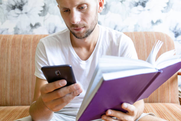 istock young guy with a smile looks into the screen of a smartphone while sitting on a sofa 1163249541