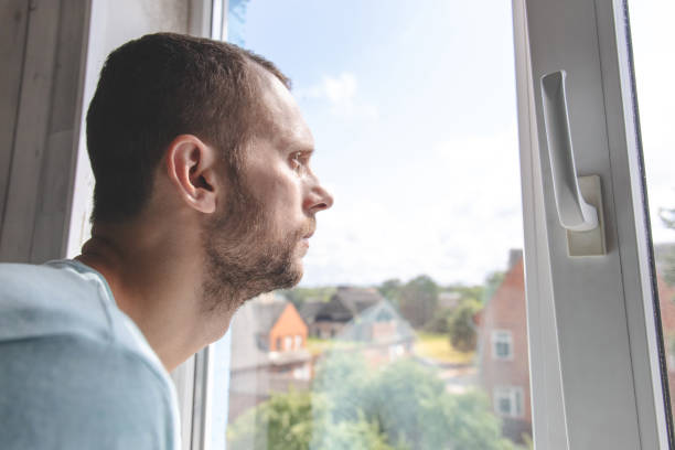 istock young guy looks out the window on a sunny day 1163249563