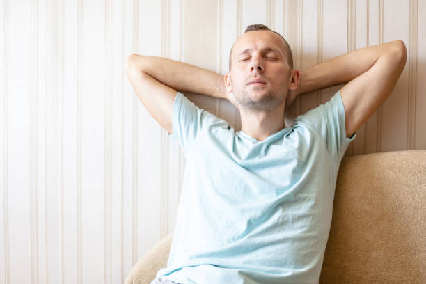 istock the guy is resting at home on the sofa with his eyes closed, his hands behind his head 1163249577