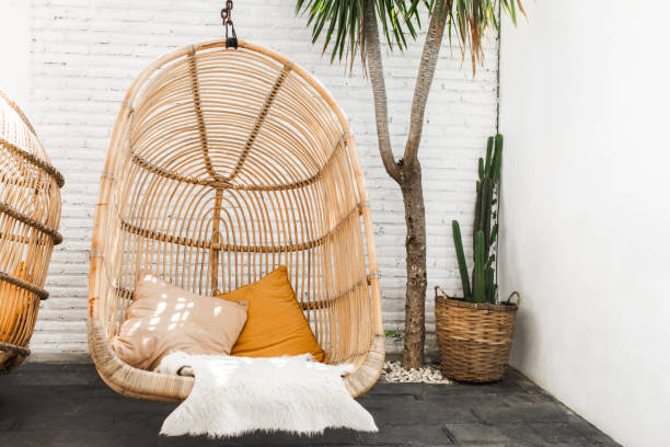 Wicker rattan hanging chair in loft cafe. Eco friendly furniture style and concept. Orange pillows and soft fur on chair. Hipster cafe in mexican style with cactus and palm. stock photo