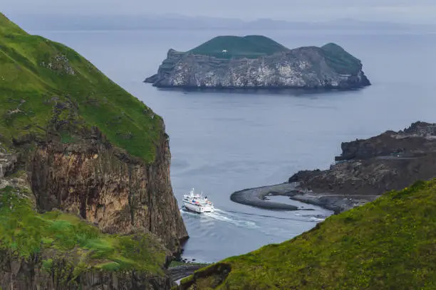 Photo of Passenger ferry in Vestmannaeyjar port, Iceland. Ellidaey island on background. Aerial view. Nordic landscape.