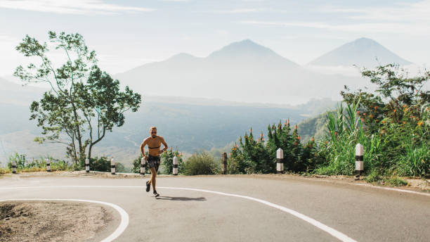 homem que funciona em topless no subida na estrada asfaltada no tempo quente do verão. opinião panorâmico da montanha no fundo. usando monitor de frequência cardíaca torácica. - fashion shirtless caucasian one person - fotografias e filmes do acervo