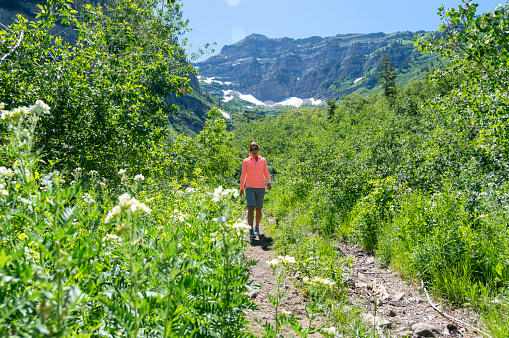 This is a view of the trail leading to Mount Timpanogos in northern Utah.  This shot was taken during the height of summer after a very wet winter and spring.  The mountains are covered in lush green foliage and some snow remains in the shadowy crevices of the peaks.  A female model is seen on the trail her back to the camera.