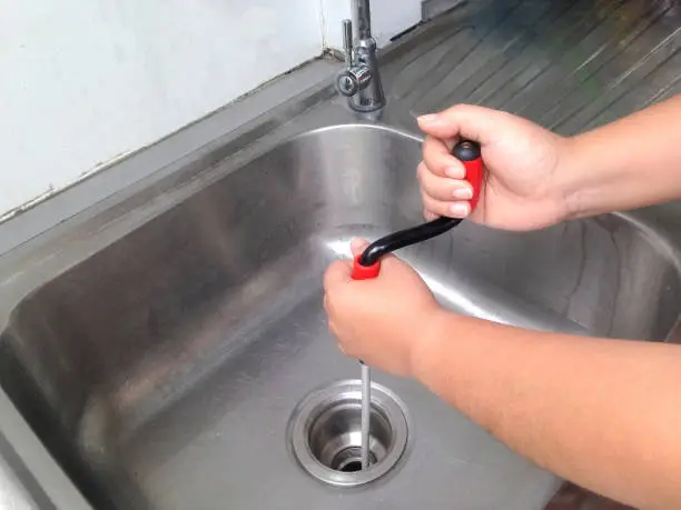 Photo of Woman's hand are breaking through the pipes. Clog pipe cleaner by yourself. Flexible spring drain cleaner.