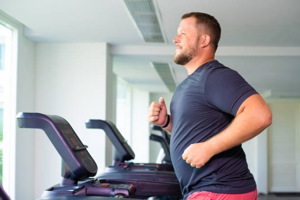 full male runs on a treadmill in a gym. concept of weight loss and sport. side view full male runs on a treadmill in a gym. concept of weight loss and sport. side view overweight man stock pictures, royalty-free photos & images