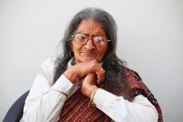 Authentic portrait of an Indian Origin Elderly Women, who is empowered and a strong lady like head of the family, wearing traditional Indian dress of red color with veil and thinking deep and posing thoughtful. She is in her 70s and still work everyday without fail and is hoping for the better days. This portrait is kinda very typical face or may say a Poster Face of almost every elderly women of rural India. Main subject is isolated well from the background.
