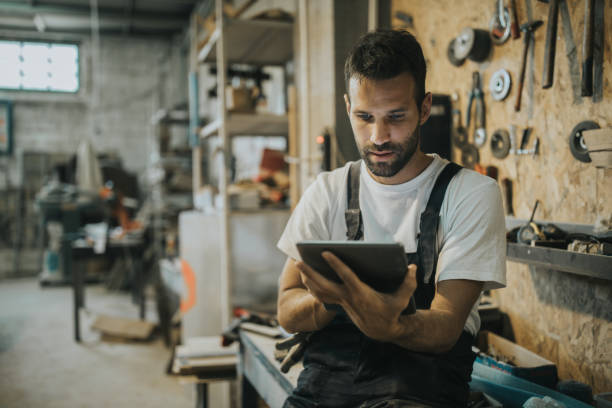 młody pracownik fizyczny korzystający z cyfrowego tabletu w warsztacie. - men mechanic manual worker craftsperson zdjęcia i obrazy z banku zdjęć