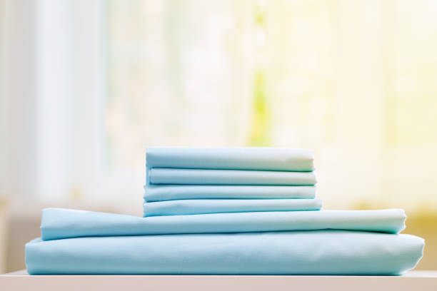 istock Close-up of blue clean bedding on a blurred background. A stack of folded new bed sheets on the table. Sunlight from the window. 1163289476
